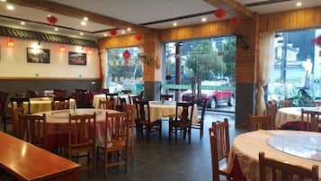 A restaurant with multiple tables and chairs, large windows, and a view of the outside.
