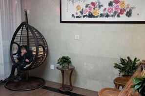A room with a hanging chair, a small table with a plant, and a framed floral artwork on the wall. - Ruyilou Hostel (Yueqing)
