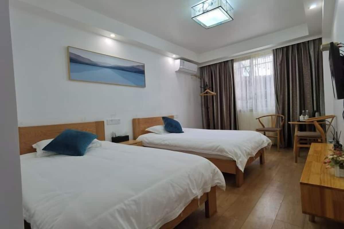 A hotel room with two beds, a desk, a chair, a painting on the wall, and a window with curtains.