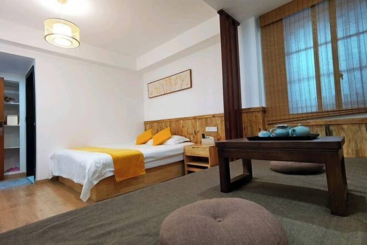 A hotel room with a bed, a wooden headboard, a nightstand, a table, and a window with blinds.