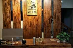 Un comptoir d’accueil avec un panneau arrière en bois, un ordinateur portable, une plante et un panneau illustrant une montagne et un bâtiment.