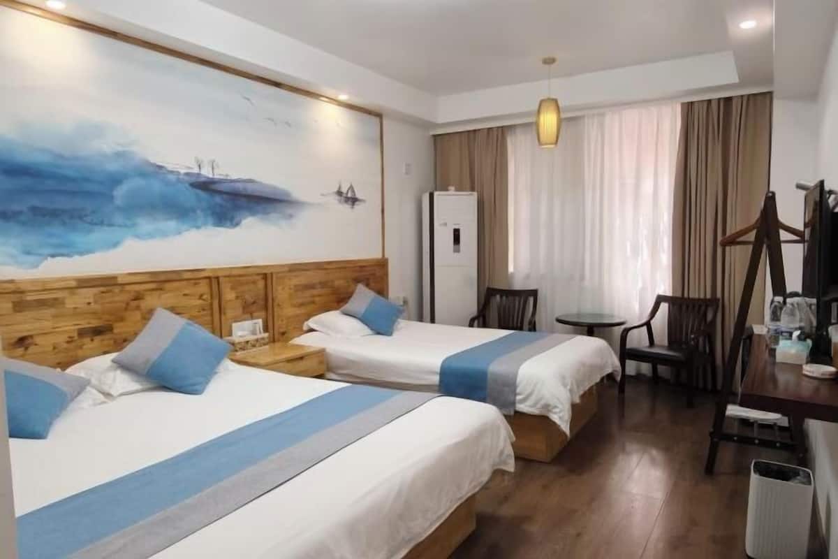 A hotel room with two beds, a wooden headboard, a painting, a desk, a chair, and a small table.