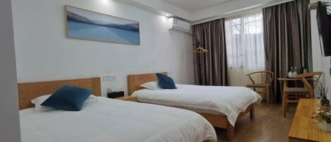A hotel room with two beds, a desk, a chair, a painting, and a window with curtains.