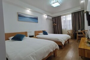 Quarto de hotel com duas camas, uma escrivaninha, uma cadeira, um quadro e uma janela com cortinas.