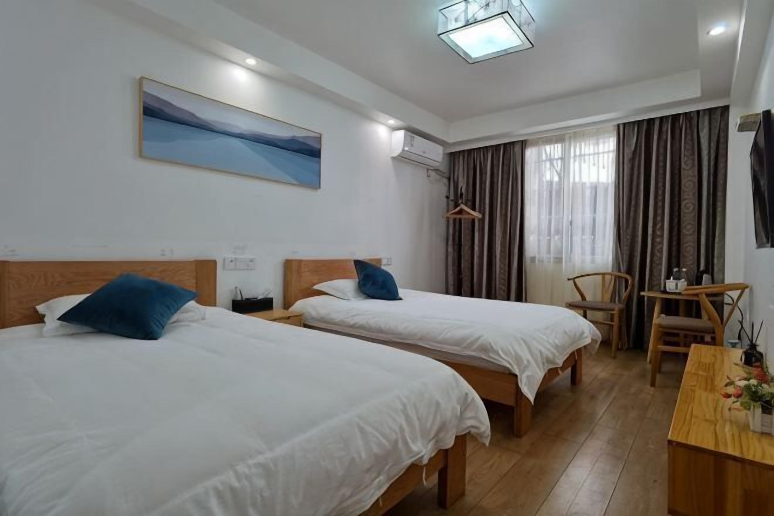 Une chambre d’hôtel avec deux lits, un bureau, une chaise, un tableau et une fenêtre avec des rideaux.