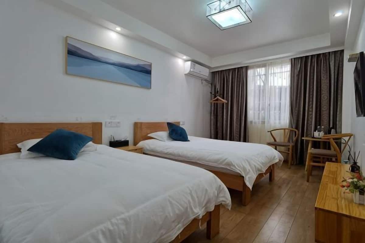 A hotel room with two beds, a desk, a chair, a painting, and a window with curtains.