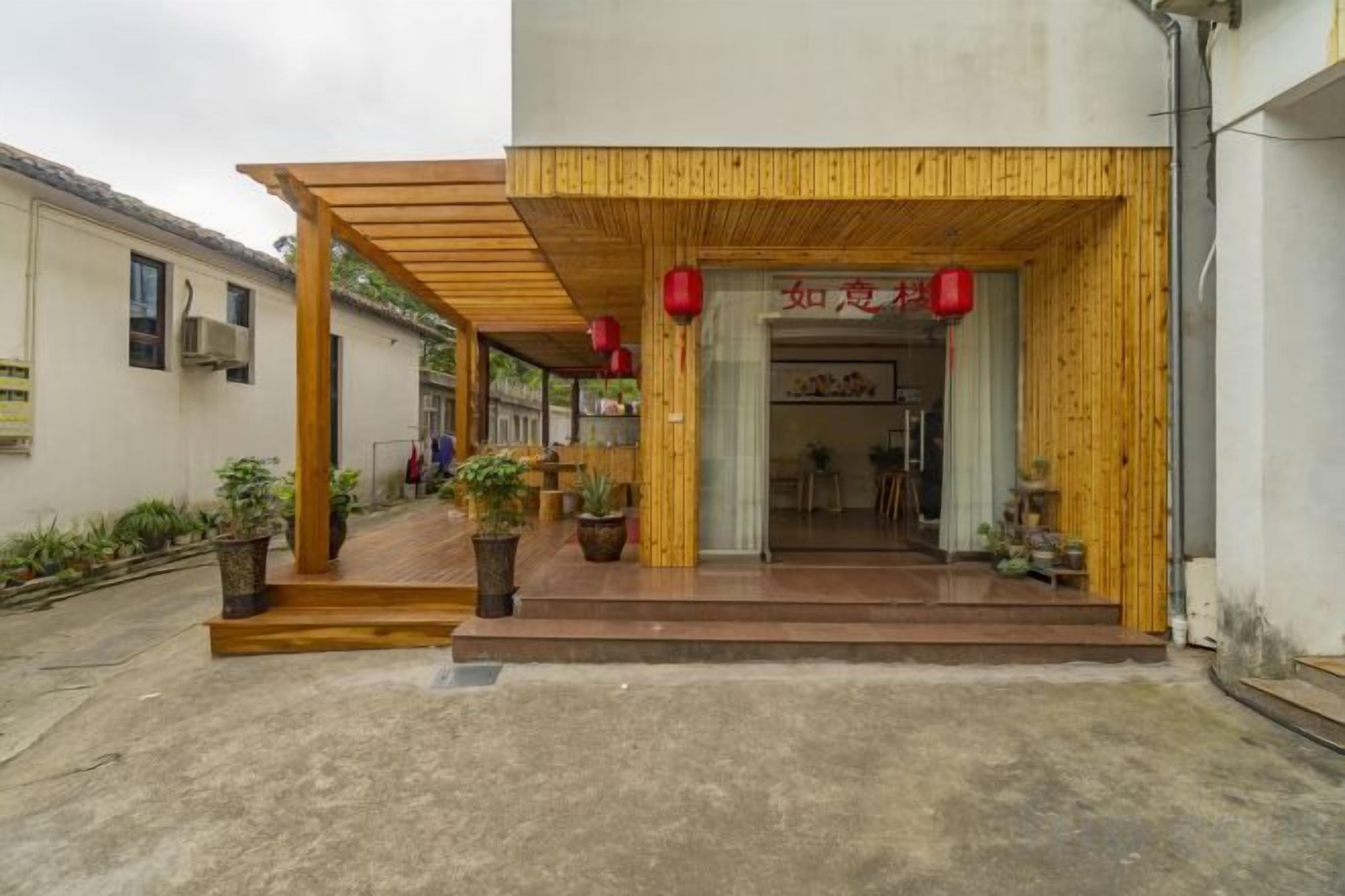 A building entrance with a wooden overhang, potted plants, and a red lantern.