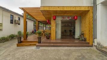 A building entrance with a wooden overhang, potted plants, and a red lantern.
