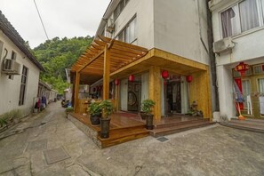 Un bâtiment doté d’un porche en bois, de plantes en pot et d’une enseigne rouge.