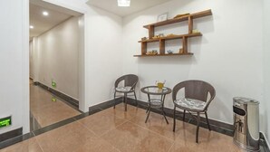 A hallway with a tiled floor, two wicker chairs, a small round table, and a trash can. - Ruyilou Hostel (Yueqing)