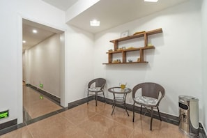 A hallway with a tiled floor, two wicker chairs, a small round table, and a trash can. - Ruyilou Hostel (Yueqing)