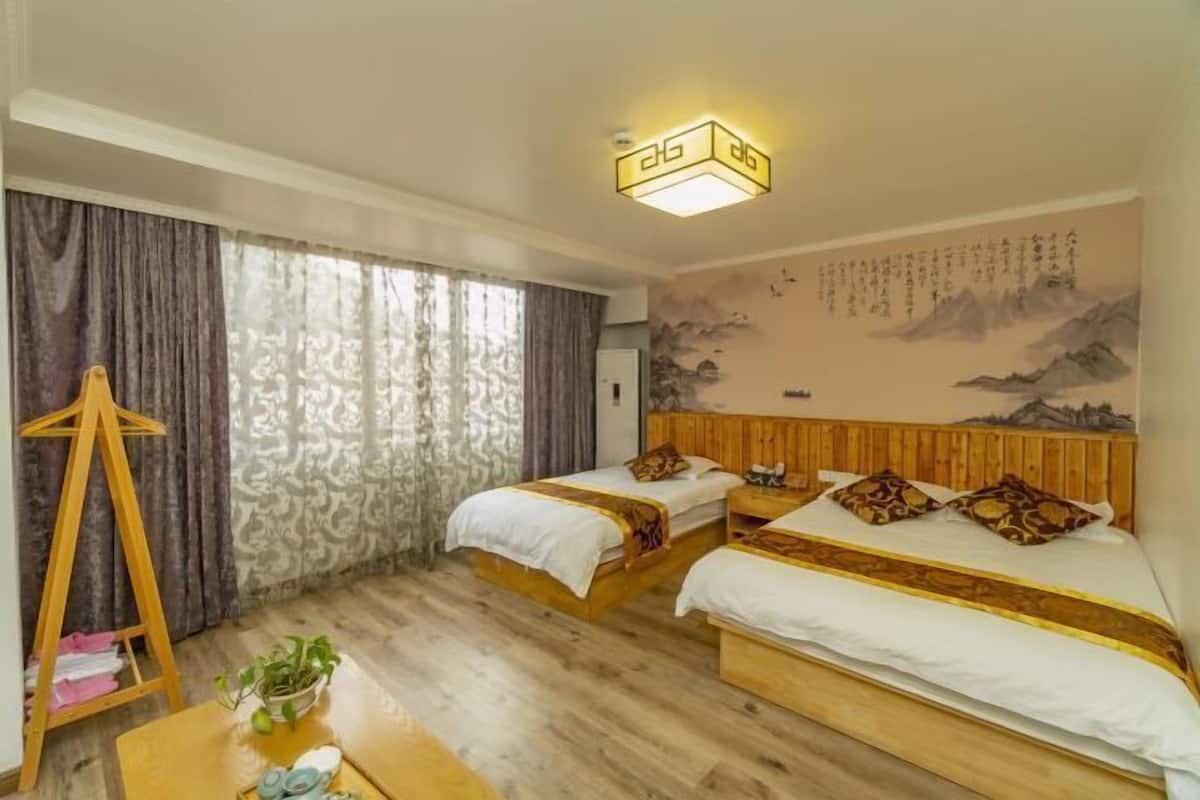 A hotel room with two beds, a wooden headboard, a desk with a plant, and a curtain.
