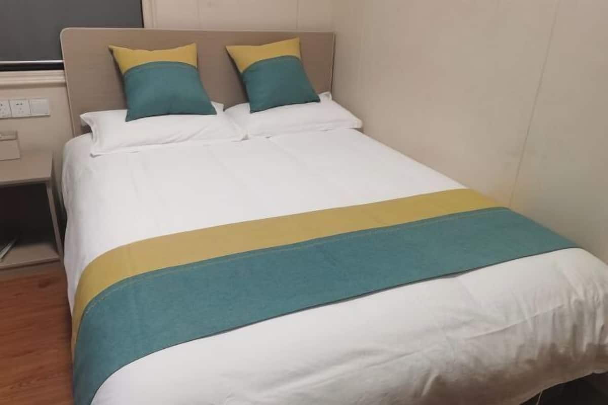 A bed with white bedding, teal and yellow pillows, and a teal and yellow bedspread.