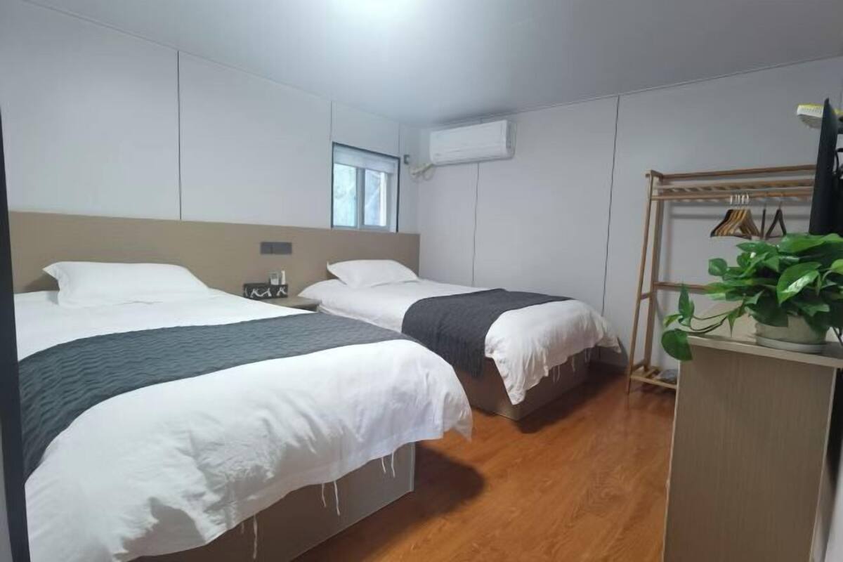 A hotel room with two beds, a wooden floor, a window, and a plant.