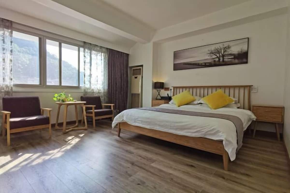A bedroom with a bed, a chair, a small table, and a window with curtains.