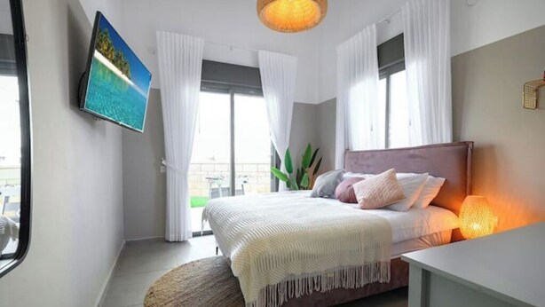 Een slaapkamer met een bed, een aan de muur bevestigde televisie en een raam met gordijnen.