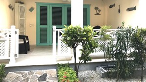 A covered outdoor area with a white railing, a stone pathway, and potted plants.