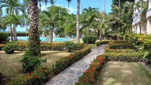 A well-maintained garden with a stone pathway, palm trees, and a pool in the background.