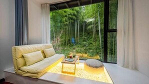 A modern living room with a sofa, a coffee table, and a view of a forest through large windows. - Xianbu Tingxia Villa (Deqing)