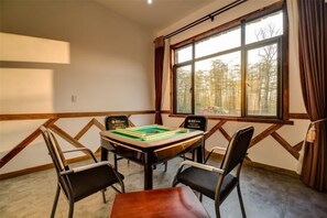 Une pièce avec une table dressée pour deux personnes, une fenêtre avec des rideaux et une vue sur les arbres.