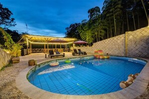 Une piscine dotée d’un espace couvert, de chaises longues et d’un jardin clôturé.