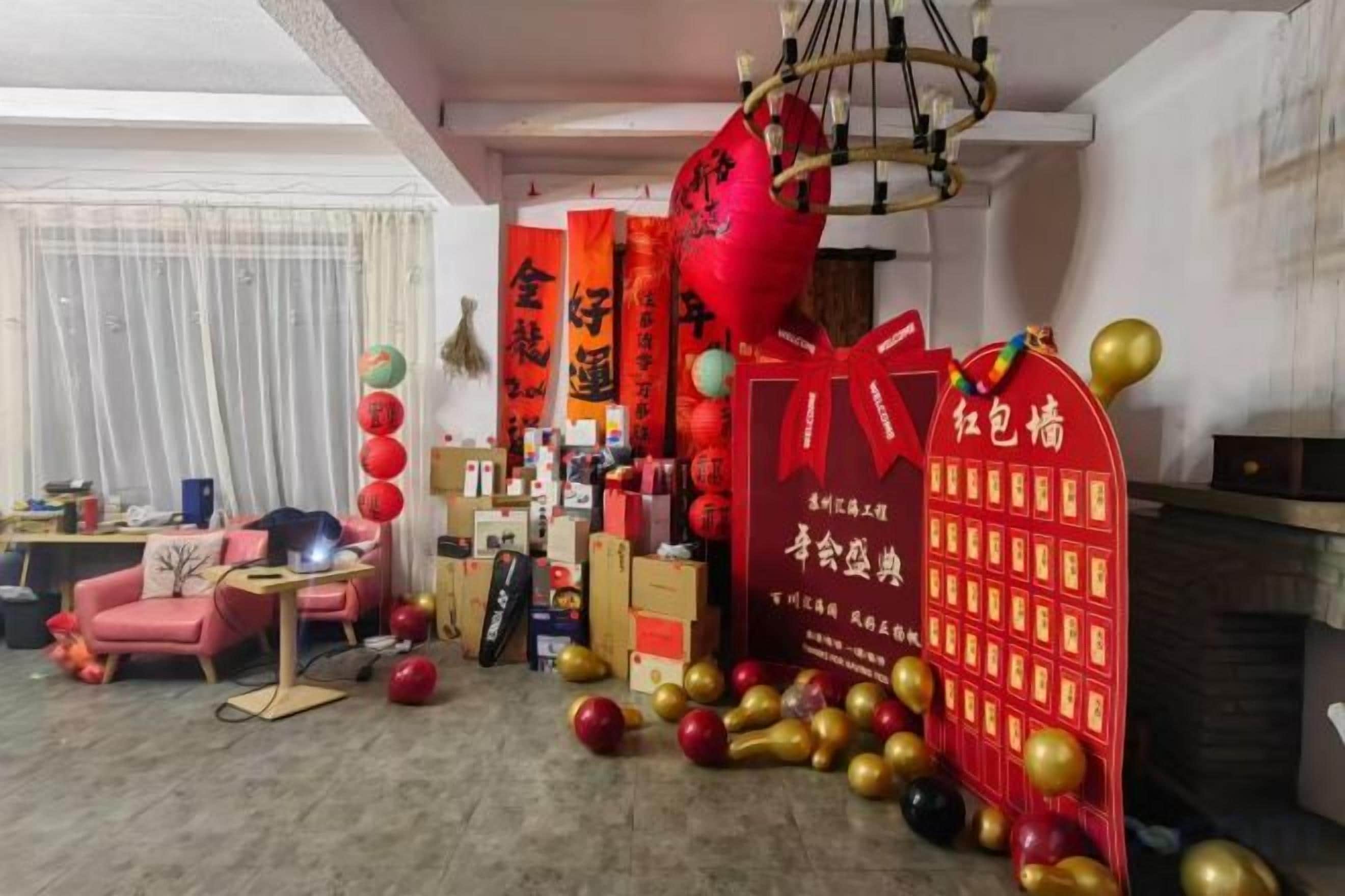 A room with a fireplace, a desk, and a chair. There are red decorations and balloons on the floor.