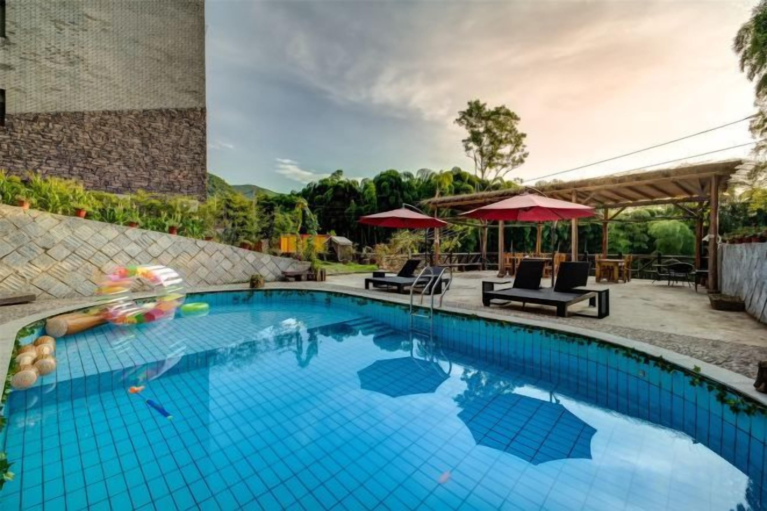 A swimming pool with lounge chairs and umbrellas, surrounded by greenery and a stone wall.