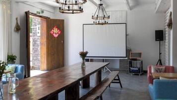 A room with a wooden table, benches, a projector screen, and a speaker.