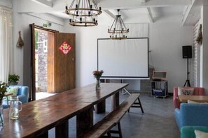 Une pièce comprenant une table en bois, des bancs, un écran de projection et un haut-parleur.