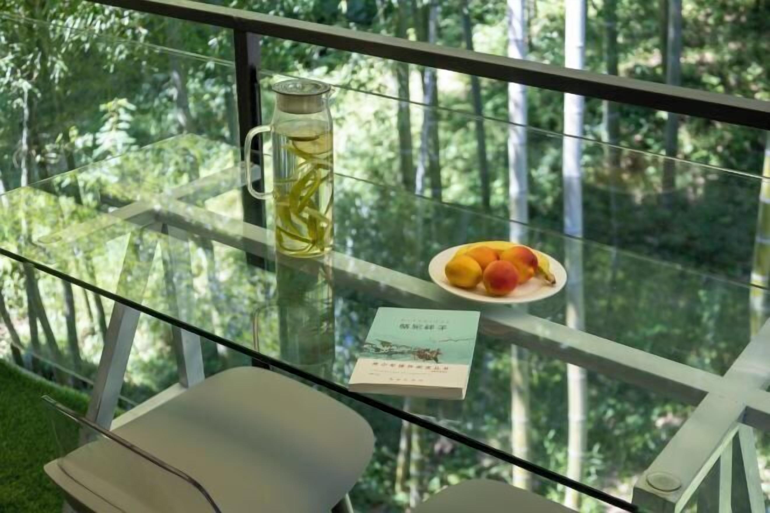 A glass table with a pitcher of water, a plate of fruit, and a book.