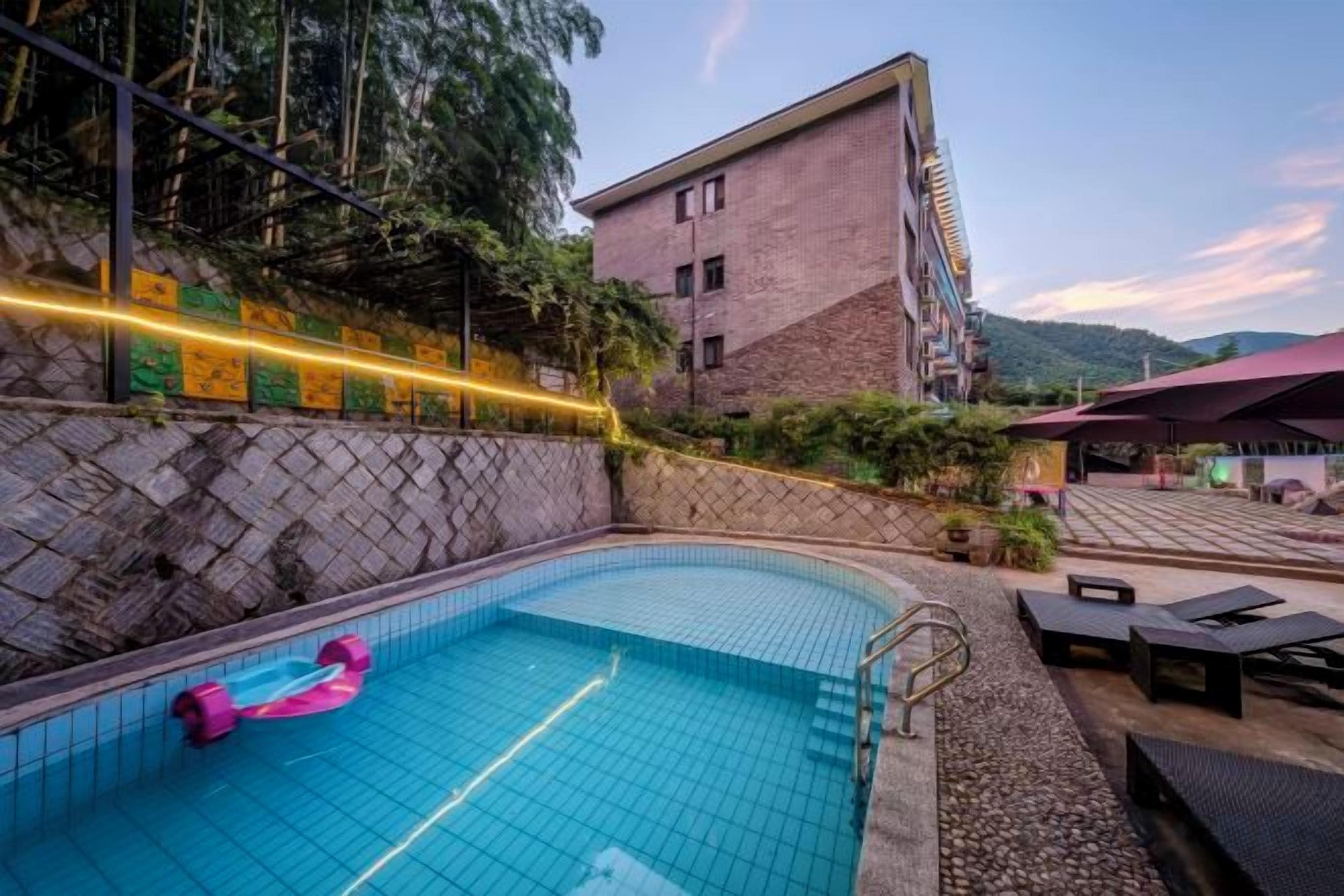 Una piscina al aire libre con un flotador rosa, rodeada por un muro de piedra y un edificio con techo inclinado.