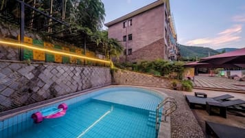Una piscina al aire libre con un flotador rosa, rodeada por un muro de piedra y un edificio con techo inclinado.