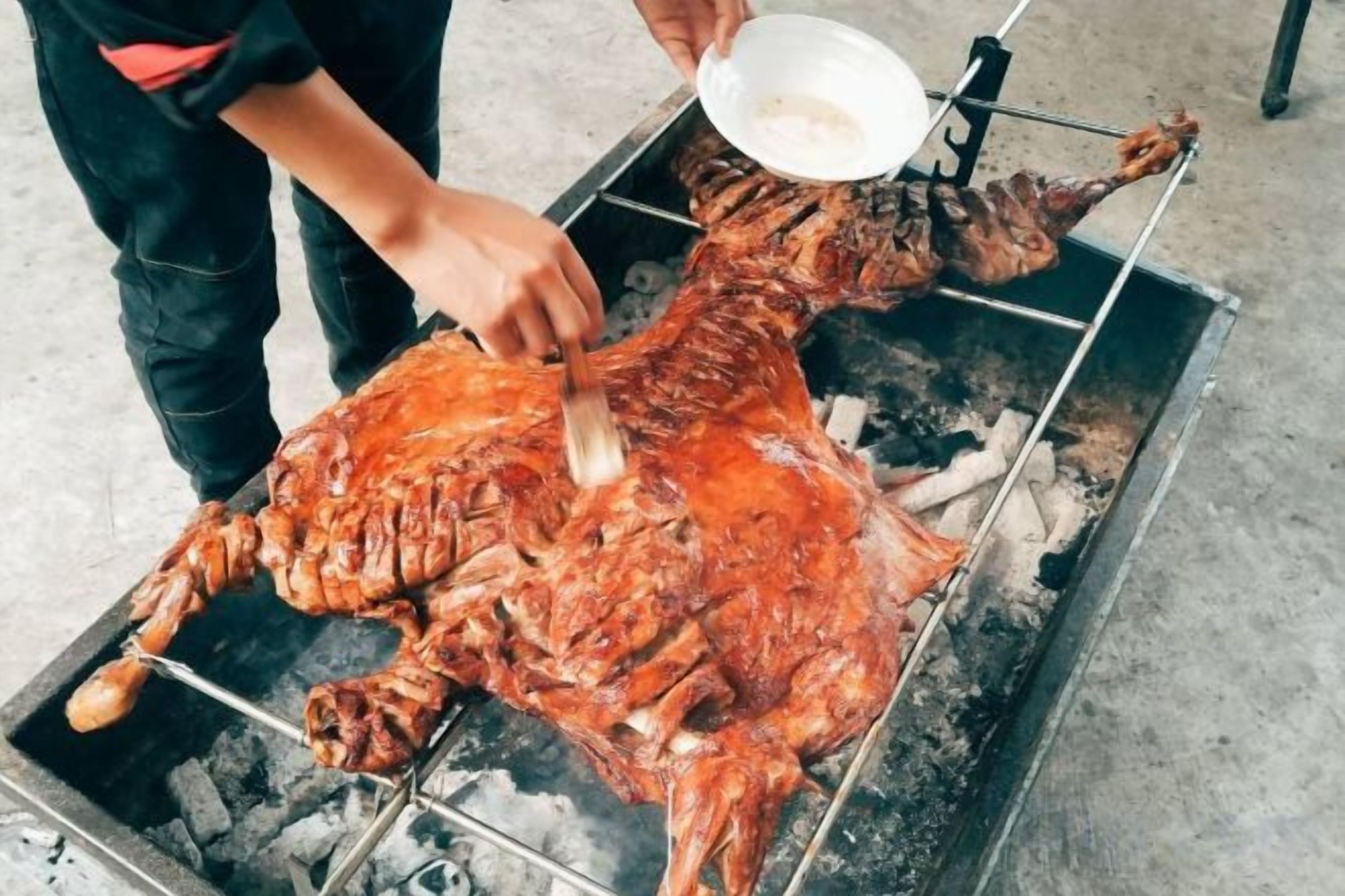 A person carving a large roasted animal on a spit over an open flame.