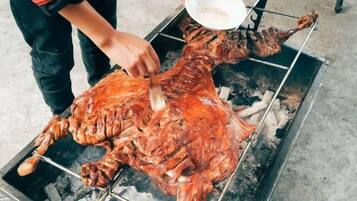 A person carving a large roasted animal on a spit over an open flame.