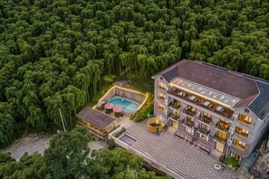 A multi-story building with a swimming pool, surrounded by dense greenery. - Xianbu Tingxia Villa (Deqing)