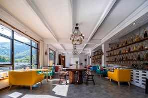 Une pièce spacieuse avec une grande table à manger, des chaises colorées, un lustre et une bibliothèque remplie de livres.