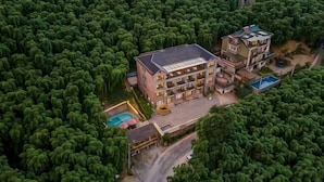 A multi-story building surrounded by dense greenery, with a swimming pool and a covered outdoor area. - Xianbu Tingxia Villa (Deqing)