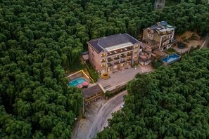 A multi-story building surrounded by dense greenery, with a swimming pool and a covered outdoor area. - Xianbu Tingxia Villa (Deqing)