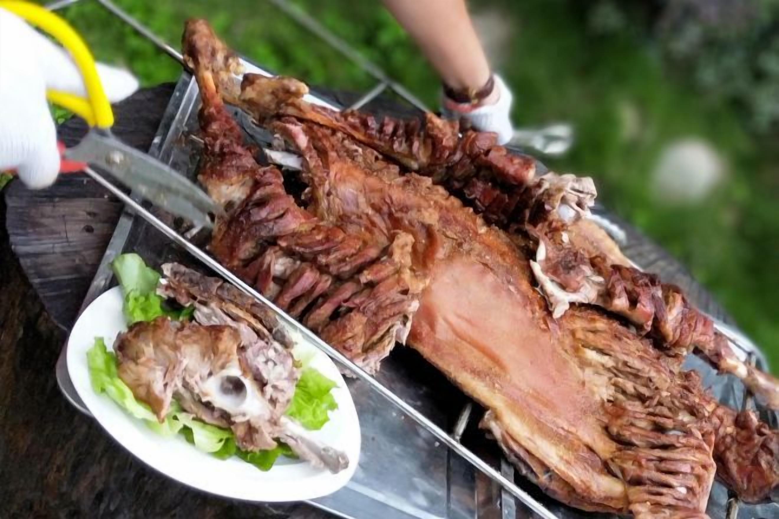 A roasted whole animal on a grill with a plate of greens beside it.