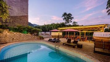 A swimming pool with lounge chairs and umbrellas, surrounded by a brick wall and vegetation.