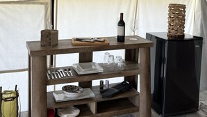 A tent with a wooden table holding a bottle of wine, glasses, and cutlery. There is a black refrigerator and a woven basket on the table. - Heritage Ranch 'Rainbow' Glamping Tent (12) (Bozeman)
