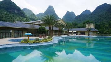 A resort with a swimming pool, palm trees, and mountainous backdrop.