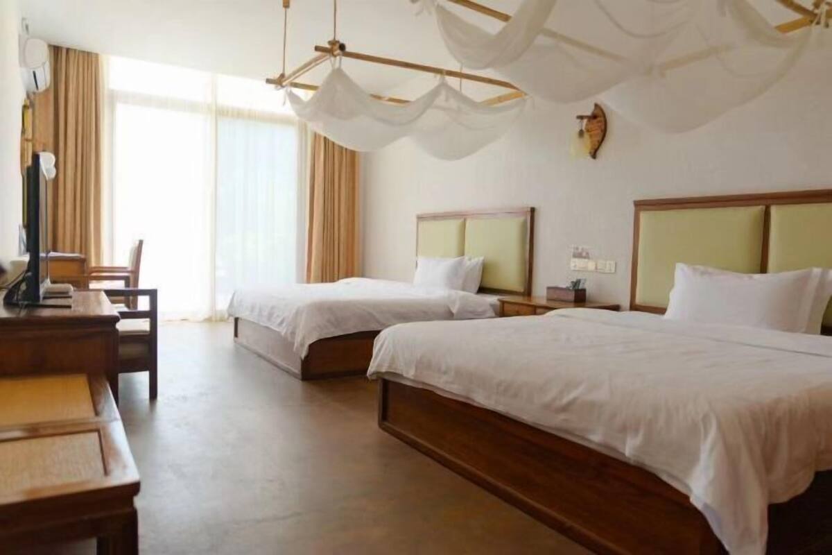 A hotel room with two single beds, a wooden desk, a chair, and a television.