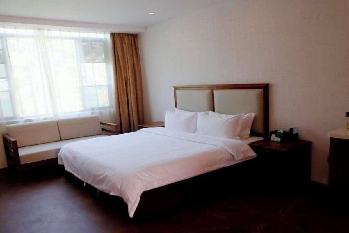 A hotel room with a large bed, a sofa, a nightstand, and a window with curtains.