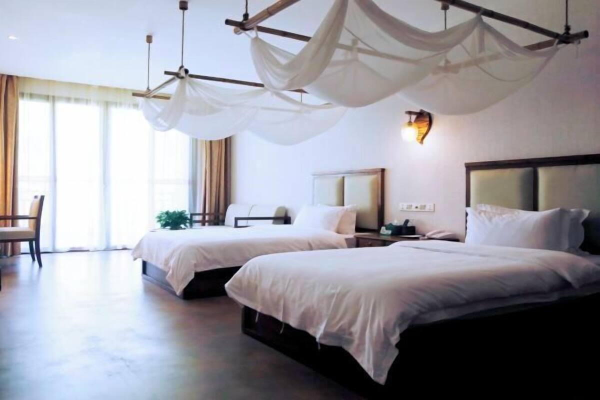 A hotel room with two beds, a large window, and a chandelier.