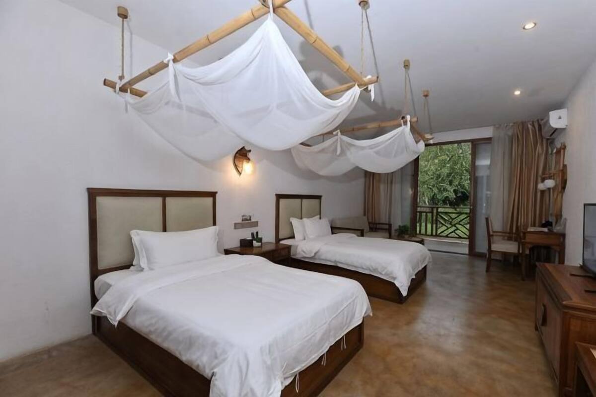 A room with two beds, a balcony, and a wooden desk.