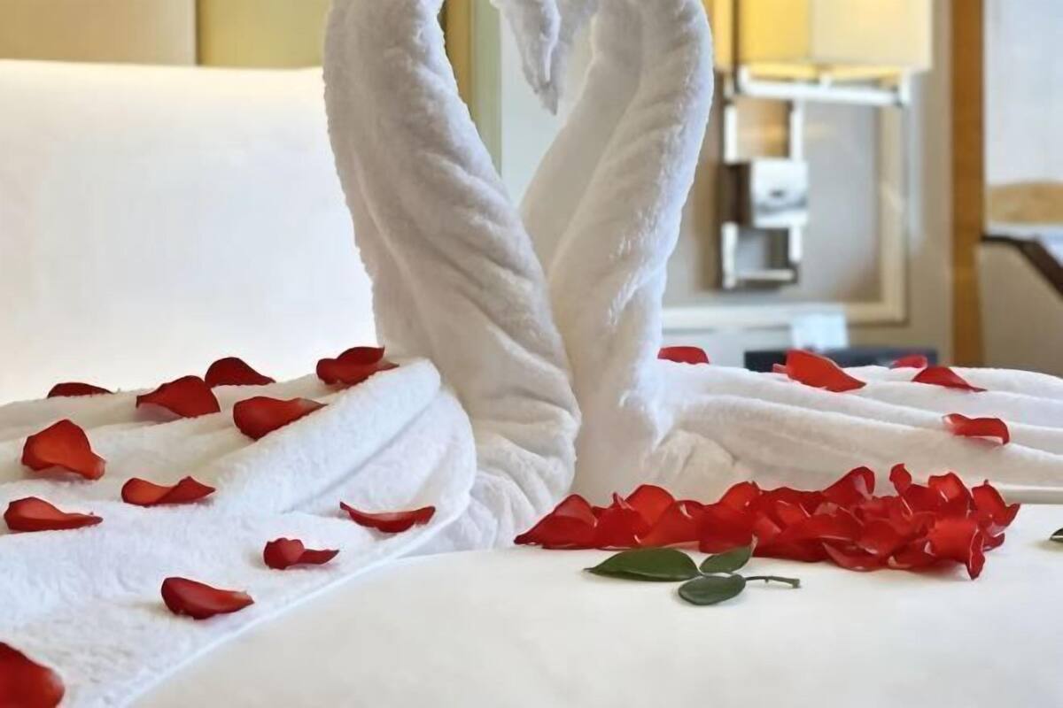 A bed with white towels and red rose petals.