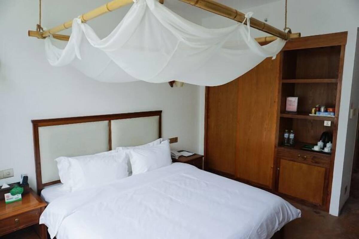 A hotel room with a bed, a wooden wardrobe, a nightstand, and a mosquito net over the bed.