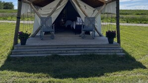 A tented accommodation with a wooden deck, two chairs, and a bed inside. - Heritage Ranch 'Big Sky' Glamping Tent (11) (Bozeman)