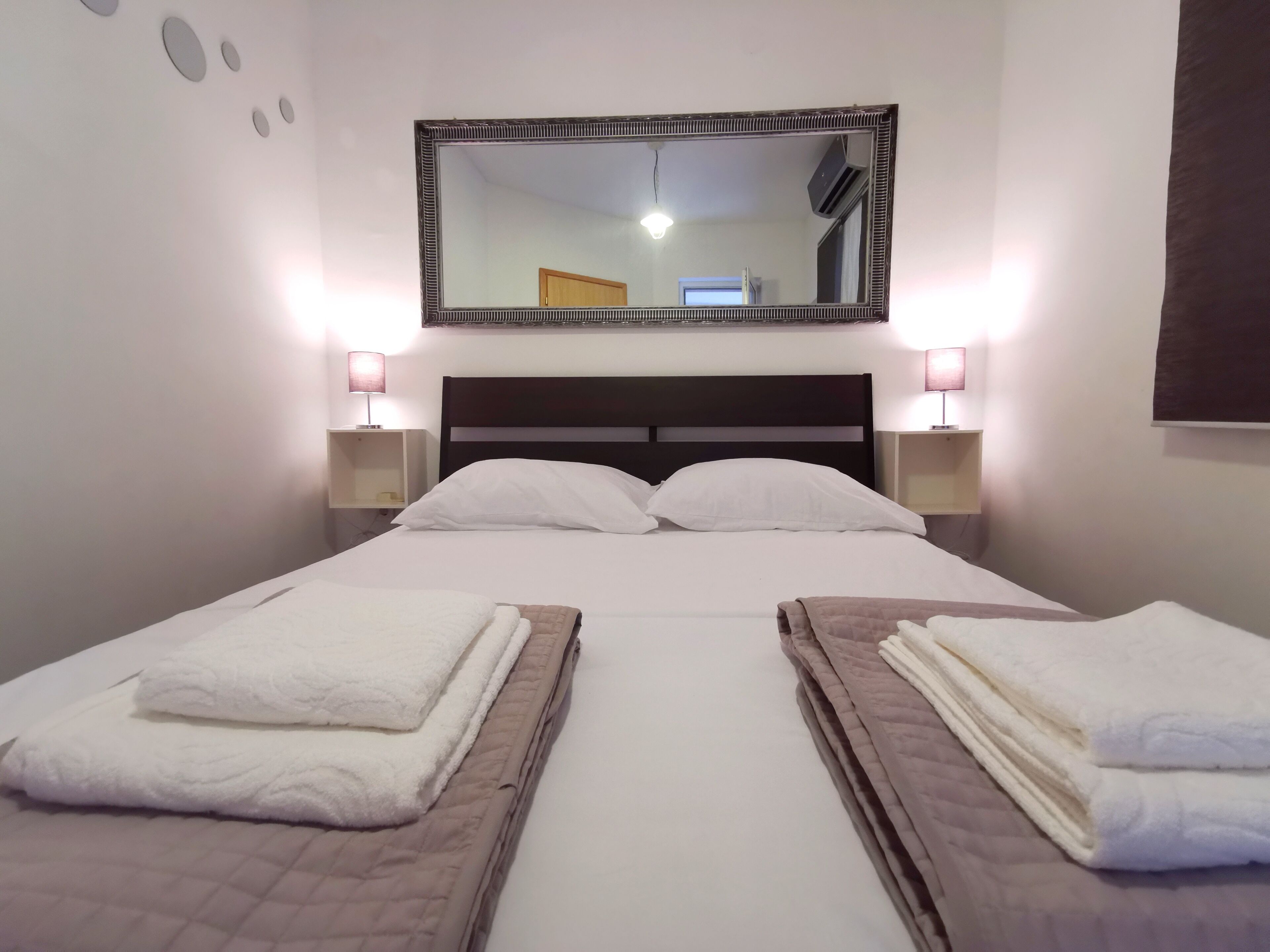 Een hotelkamer met een groot bed, twee nachtkastjes, een spiegel en een wandairconditioner.